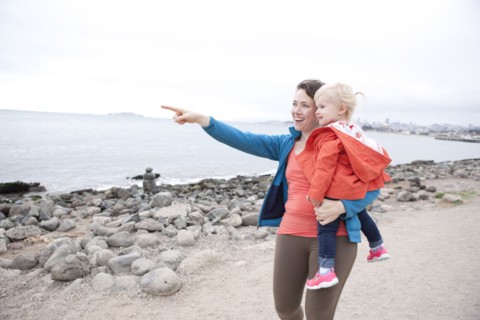 Caucasian mother holding daughter and pointing on beach