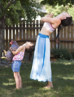 Mother and daughter practicing yoga with chicken in backyard