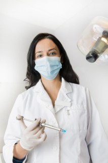 Indian dentist holding syringe by light