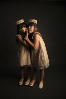 Whispering twin girls wearing crowns and princess costumes