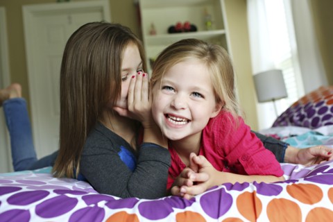 Close up of sisters whispering on bed
