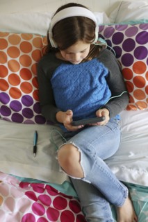 Girl listening to headphones with digital tablet on bed