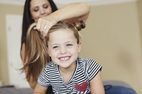 Mother styling hair of daughter on bed
