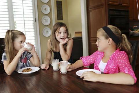 Sisters eating cookies with milk at table