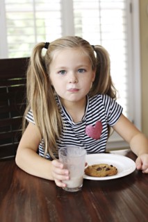 Girl eating cookies with milk mustache at table