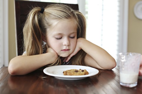 Girl staring at cookie with milk at table