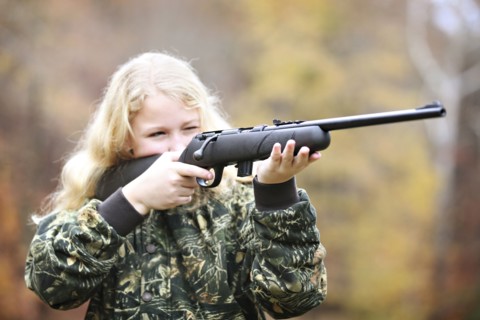 Girl in camouflage aiming rifle in forest