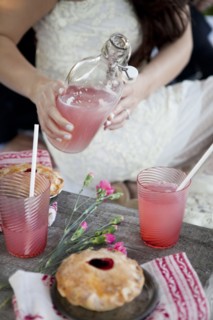 Woman pouring pink lemonade into glasses on wooden table
