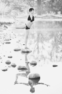 Woman in lingerie practicing yoga on rock in still pond