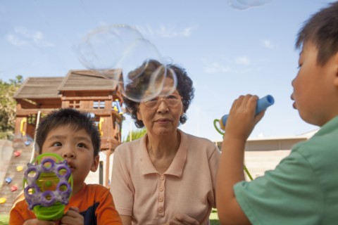 Asian grandmother and grandsons blowing bubbles outdoors
