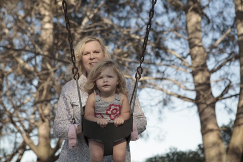 Grandmother pushing granddaughter on swing at playground