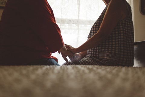 Older woman holding hand of daughter on bed
