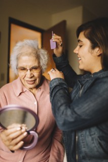 Granddaughter combing hair of grandmother holding mirror