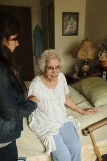 Granddaughter helping grandmother out of bed
