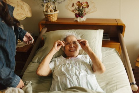 Granddaughter giving grandmother eyeglasses in bed