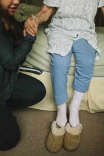 Granddaughter helping grandmother out of bed into slippers