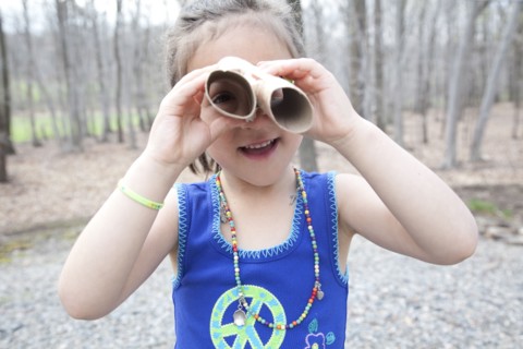 Caucasian girl playing with cardboard tubes in forest