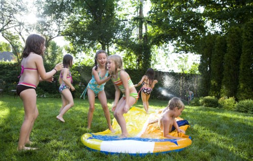 Children playing on water slide in backyard