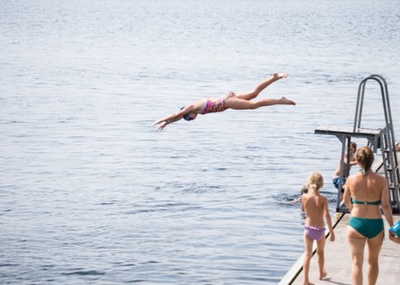 Caucasian girl jumping from diving board into lake