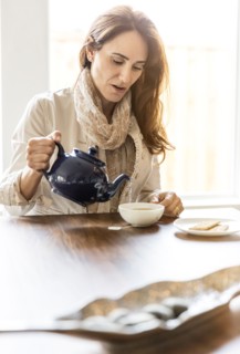 Caucasian woman pouring cup of tea at table