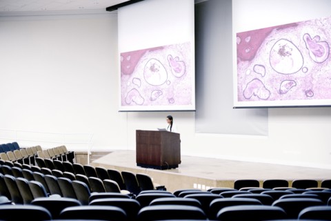 Armenian doctor speaking at podium in empty classroom