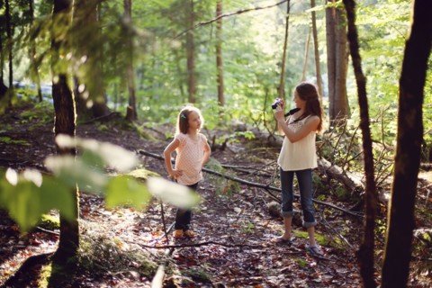 Caucasian girl photographing sister in forest