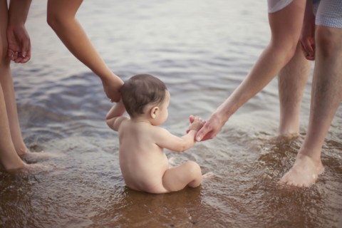 Parents helping baby sit in lake