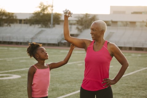 Girl squeezing biceps of grandmother on football field