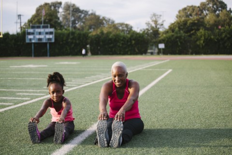 Grandmother and granddaughter stretching on football field
