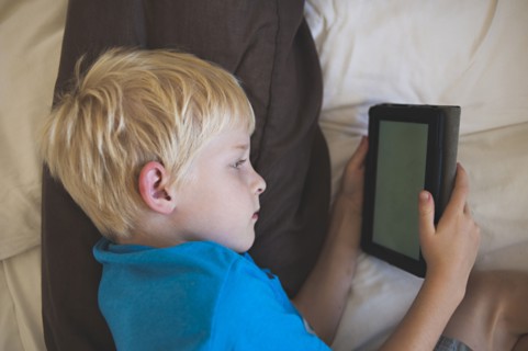 Caucasian boy reading digital tablet in bed