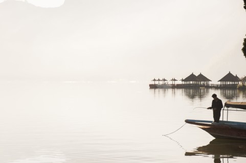 Fisherman standing in boat on still remote lake