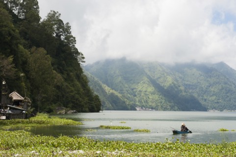 Fisherman rowing canoe on still rural lake