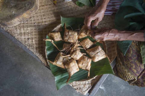 Asian man knotting woven packages on floor