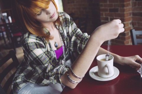 Caucasian woman sprinkling sugar in coffee