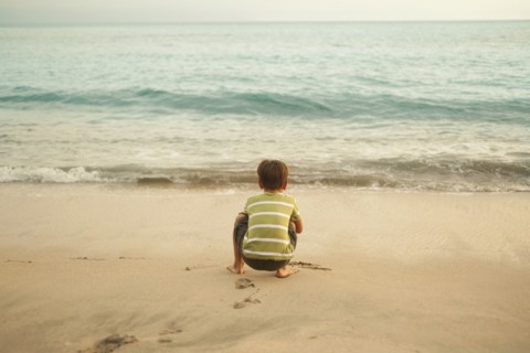 Mixed race boy squatting on beach playing