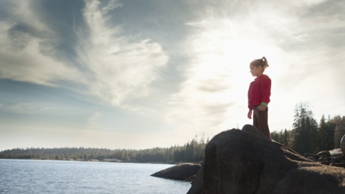 Mixed race girl standing on rock near remote lake