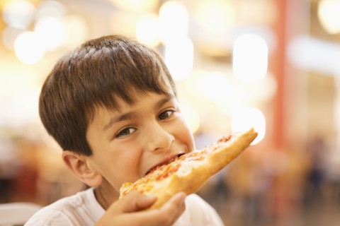Mixed race boy eating pizza in restaurant