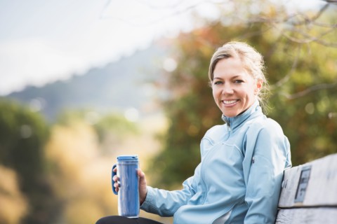 Caucasian woman having coffee on park bench