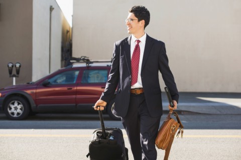 Hispanic businessman rolling luggage