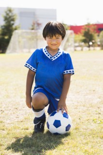 Hispanic boy with soccer ball kneeling on field