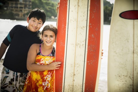 Children smiling with surfboards on beach