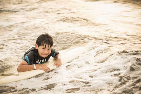Hispanic boy floating on surfboard in ocean
