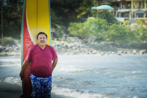 Older Hispanic man with surfboard on beach