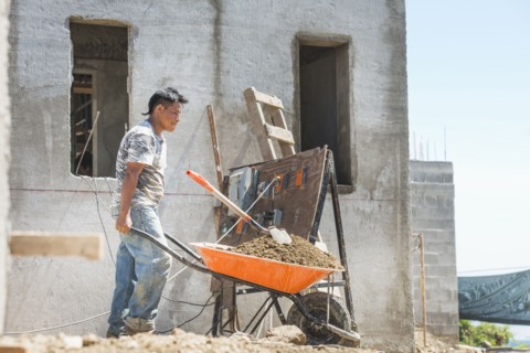 Hispanic construction worker pushing wheelbarrow at construction site