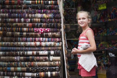 Caucasian girl admiring woven bracelets for sale in market