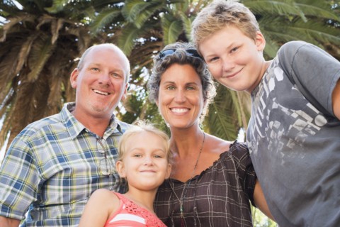 Caucasian family smiling under palm tree