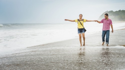 Hispanic couple playing in waves on beach