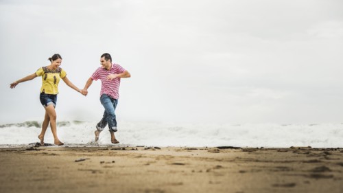Hispanic couple running in waves on beach
