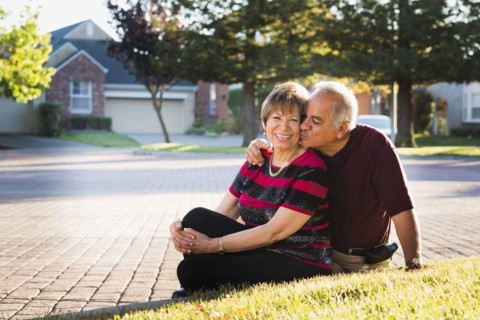 Older Hispanic couple kissing outside suburban home