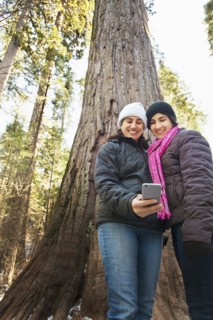Hispanic mother and daughter taking selfie in forest